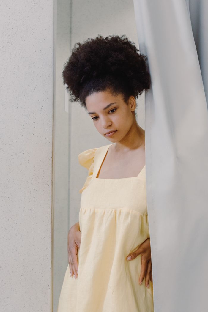 Thoughtful African American woman trying on a yellow dress in a changing room.