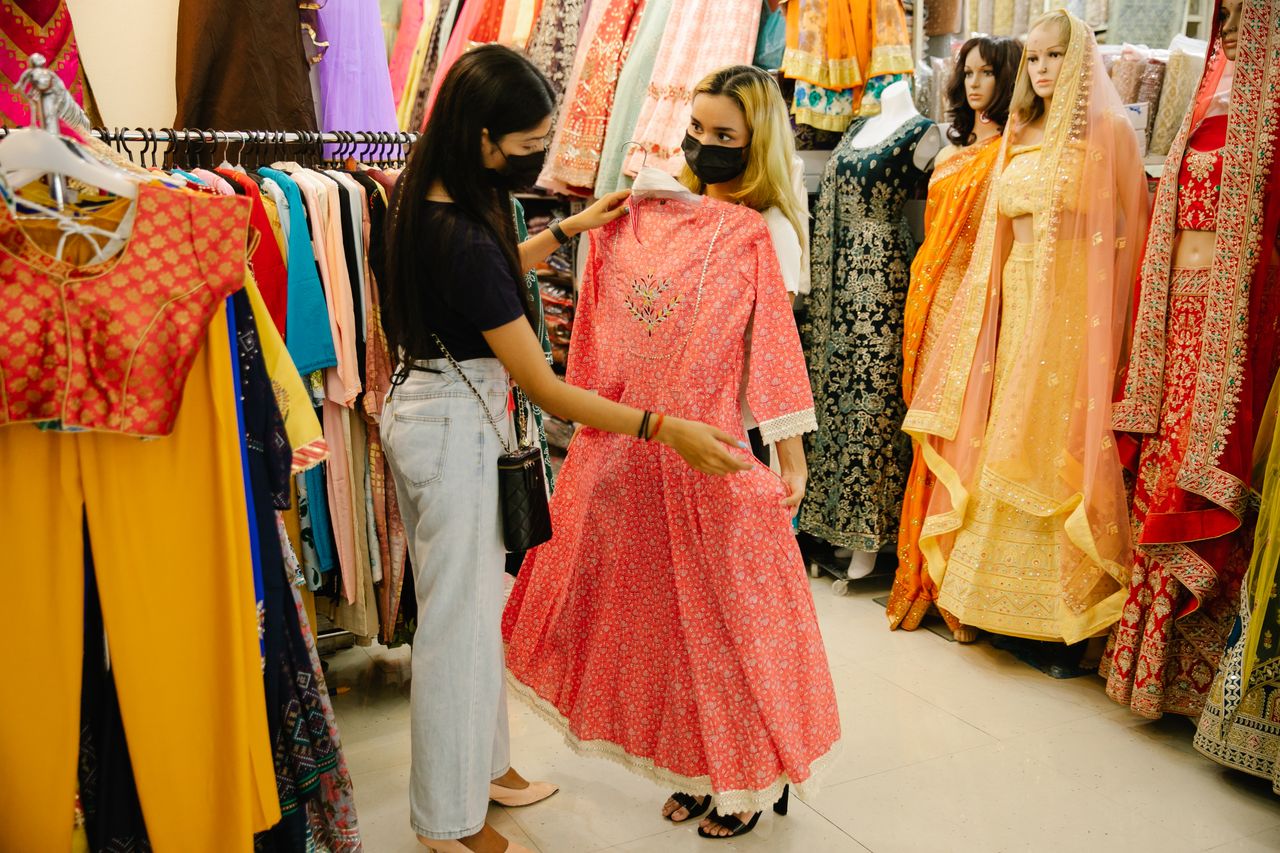 Two women browsing traditional dresses in a colorful boutique setting.